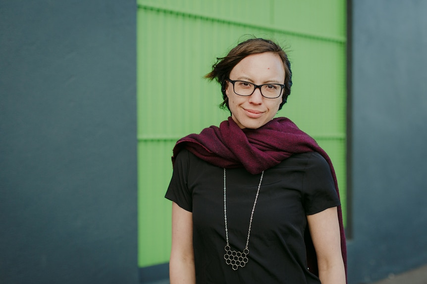 Mid-shot colour photograph of games producer Kamina Vincent standing outdoors in front of a light green and blue wall.