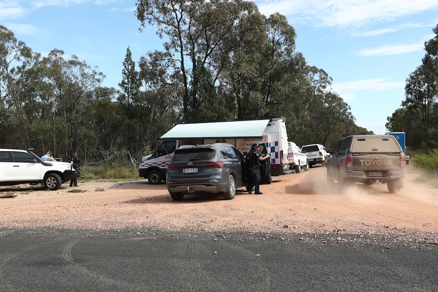 a convoy of police cars parked on a dirt road near the site of a shooting