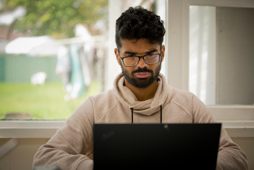 Arpit Charwal works at a computer at a table in front of a window that opens onto a backyard.