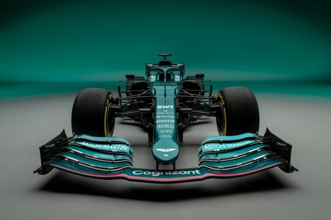 A driver-less Formula 1 car sits facing the camera in front of a metallic green background.