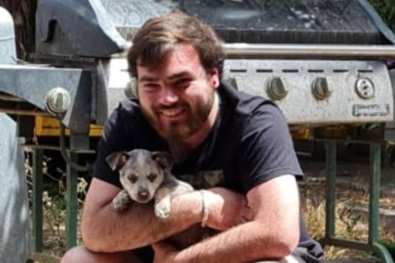 A man with a beard squatting while holding a puppy