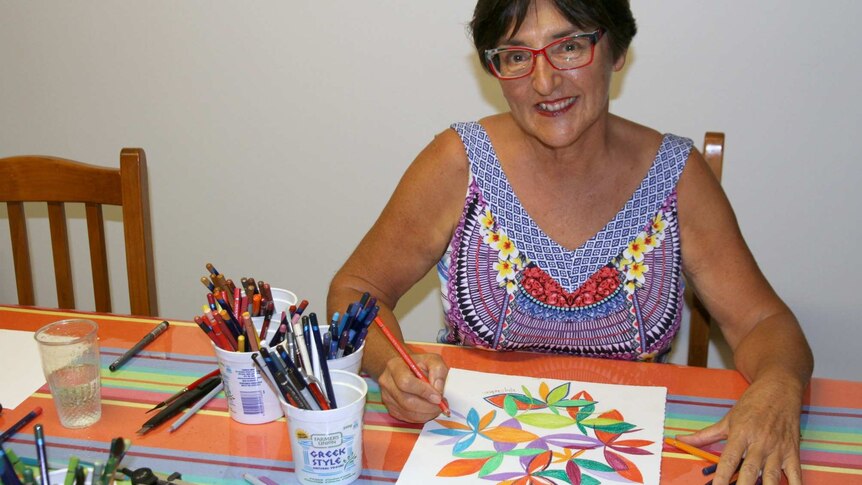 Kay Shelton sits surrounded by coloured pencils, working on a brightly coloured mandala artwork