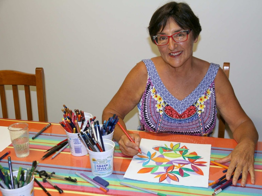 Kay Shelton sits surrounded by coloured pencils, working on a brightly coloured mandala artwork