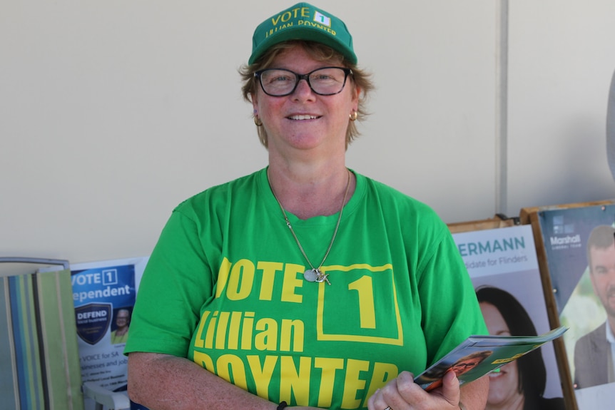 Woman wearing a a bright green cap and t-shirt that says "vote 1 Lillian Poynter"