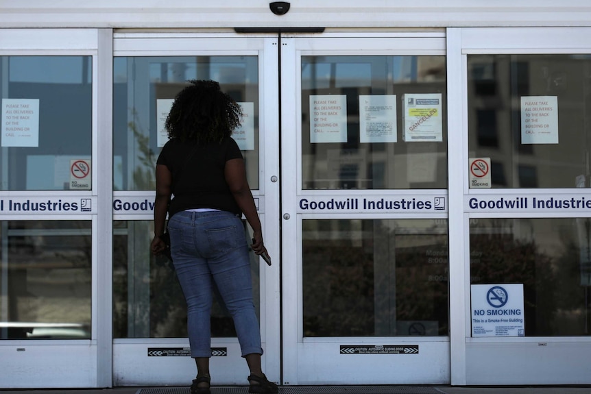 A black woman looks into the closed doors of a New Orleans unemployment office