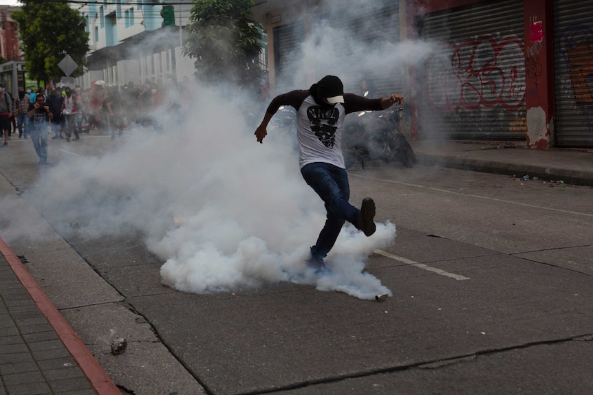 A demonstrator returns a tear gas canister fired by police near the Guatemalan Congress building