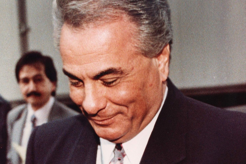 A man wearing a suit smirks as he looks down at the ground.