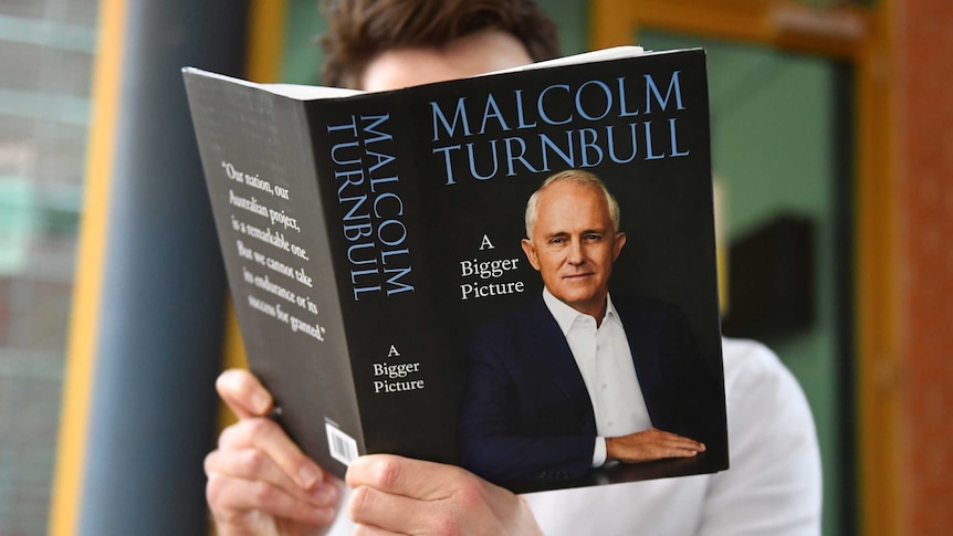 A man holds a black book which features Malcolm Turnbull on the cover.