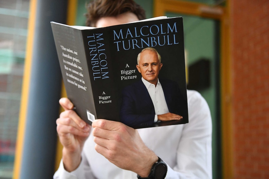 A man holds a black book which features Malcolm Turnbull on the cover.