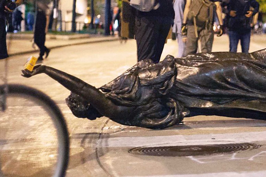 Statue of person with right arm raised lies on its side.