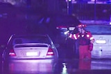A SES volunteer in a hi-visibility suit shining a torch at a car partially submerged in water