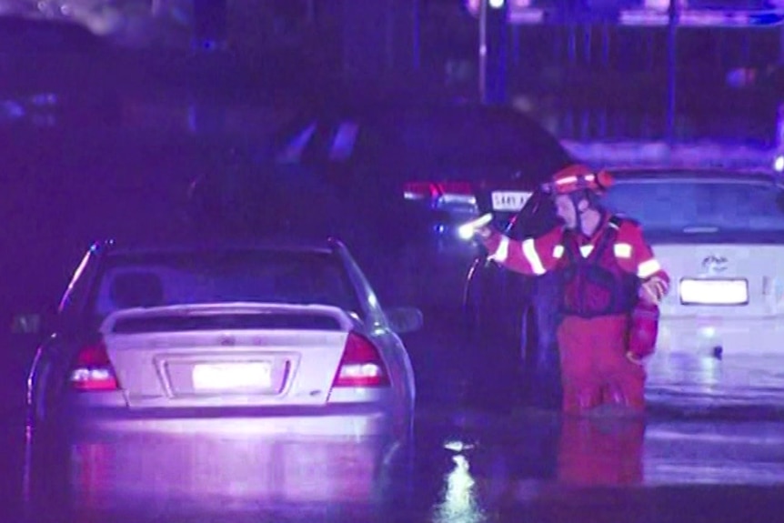 A SES volunteer in a hi-visibility suit shining a torch at a car partially submerged in water