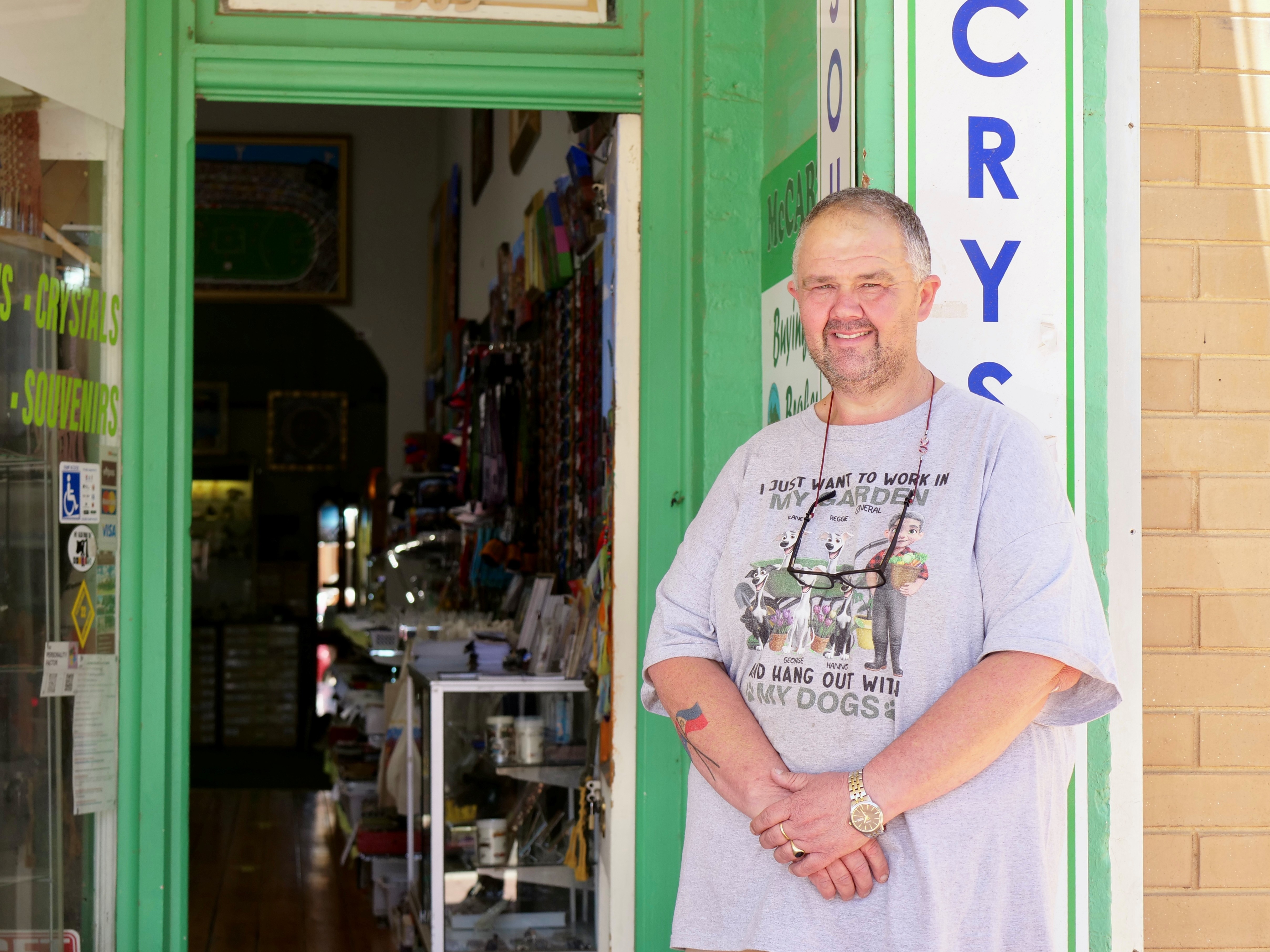 Un hombre con camisa gris se encuentra frente a la puerta de una tienda.