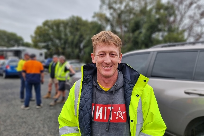 A man wearing a bright green jacket stands near a vehicle. He is smiling