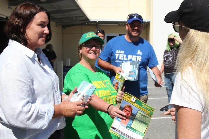 Three people hand out state election flyers, and a woman with blond hair and a black cap stands with her back to the camera.