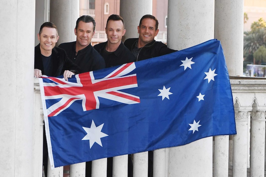 Human Nature stand on a balcony with Greek columns holding an Australian flag