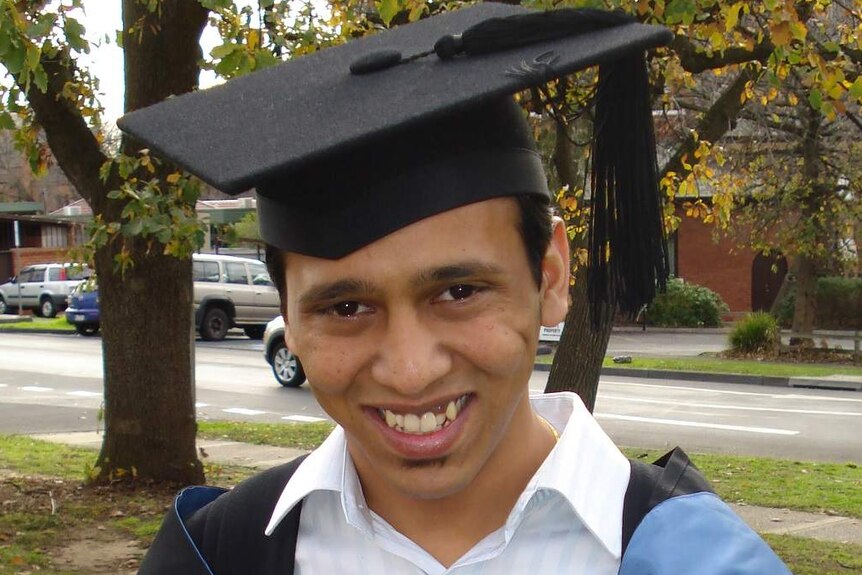 Rootvij Kadakia smiles, wearing a university graduation hat and gown as he stands on a leafy lawn.