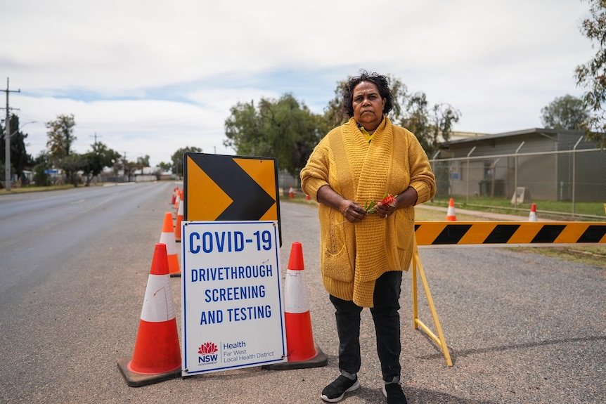 A woman stands on regional street in front of a COVID testing sign.
