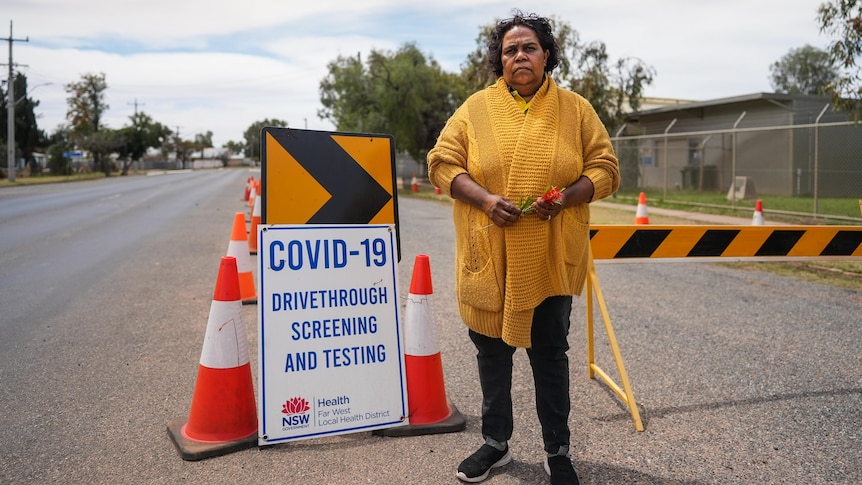 A woman stands on regional street in front of a COVID testing sign.
