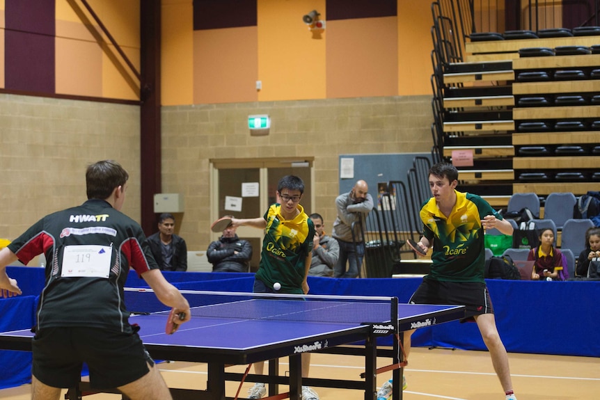 One boy at one of a table tennis table with two at the other end serving.