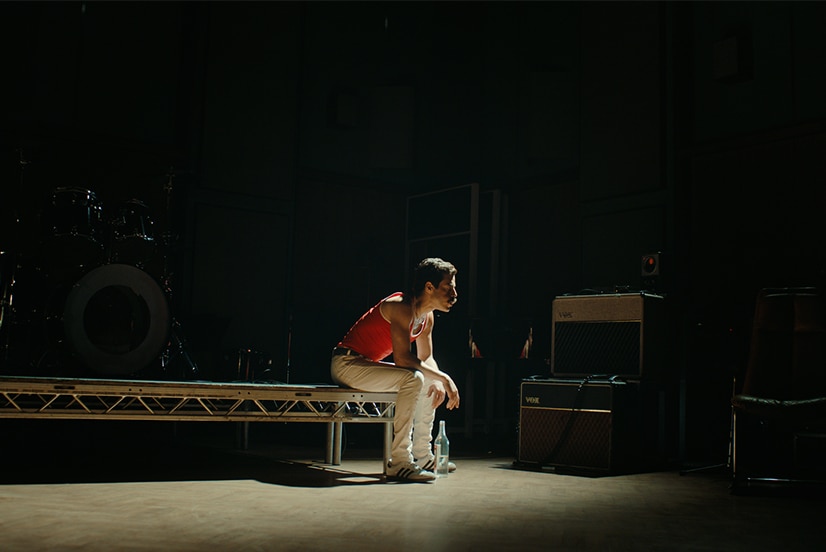 Colour still of Rami Malek sitting alone on stage riser as Freddie Mercury in 2018 film Bohemian Rhapsody.