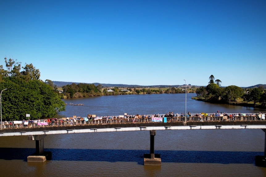An aerial shot of a bridge with people standing along the edge holding colourful signs