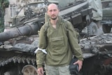 Arkady Babchenko stands in front of a destroyed army tank.