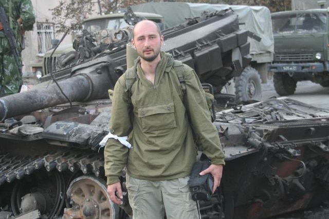 Arkady Babchenko stands in front of a destroyed army tank.