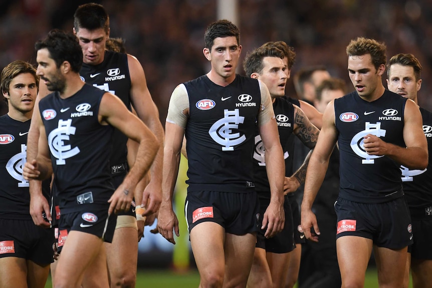 Carlton players look down as they walk off the field at half-time