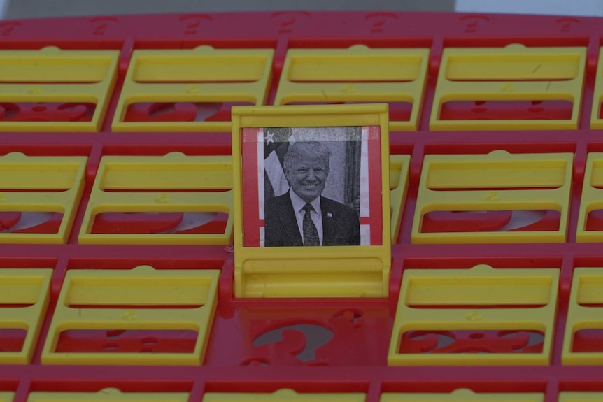 The headshot of a smiling politician in a suit sits in the frame of a board game