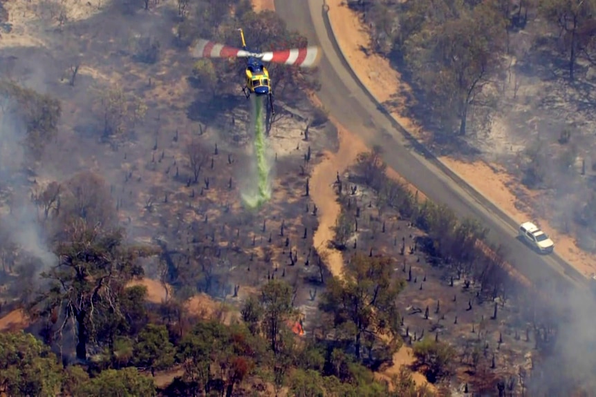 A helicopter drops green water onto burnt bushland after a fire. 