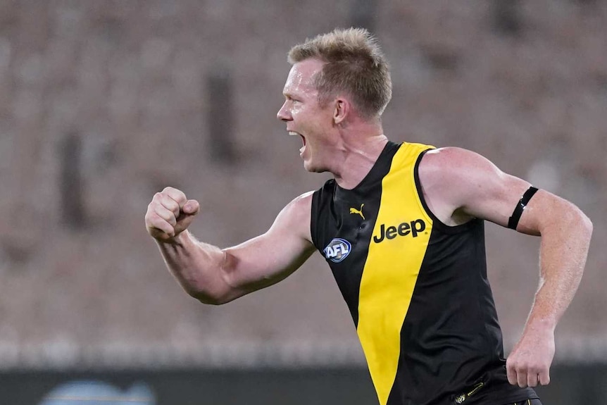 A man in a blue and yellow football uniform runs forward with his fist in the air in celebration.