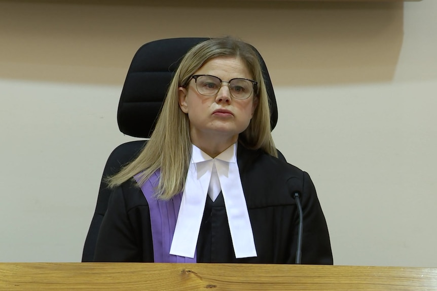 A woman dressed in a judge robe sits at the judge's bench