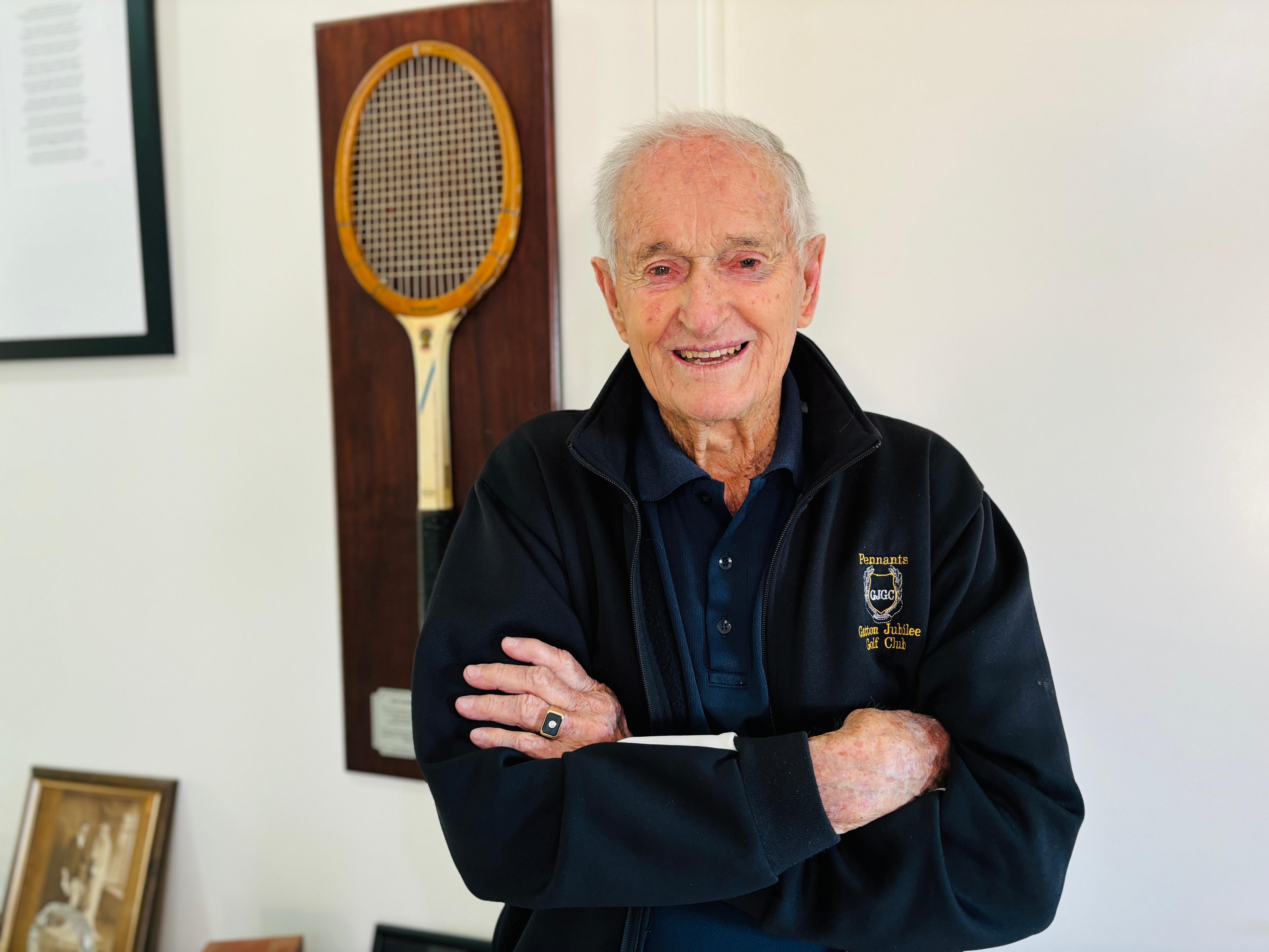 An elderly man standing with his arms crossed, smiling