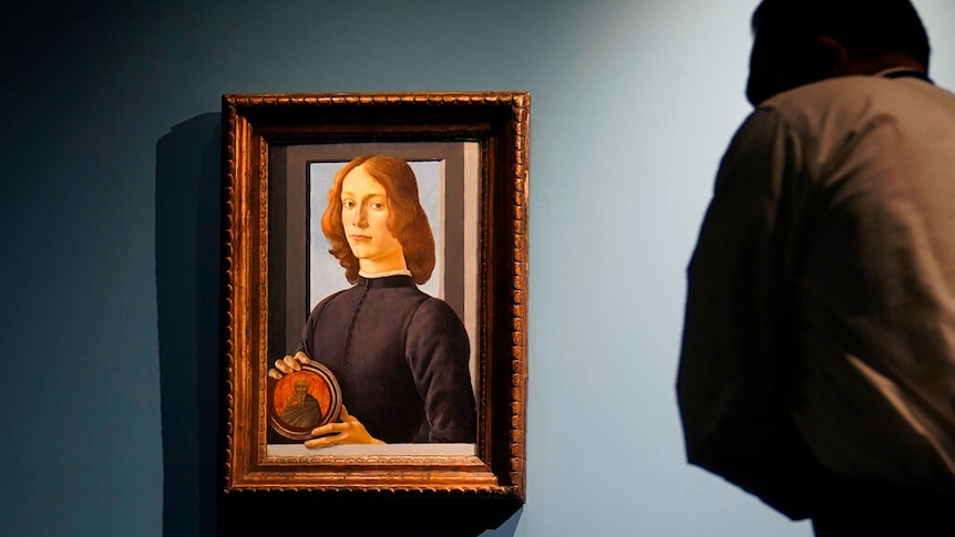 A photo of a man looking at a Renaissance portrait of a young man holding a small disc.