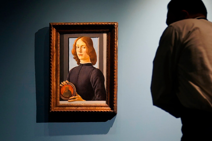 A photo of a man looking at a Renaissance portrait of a young man holding a small disc.
