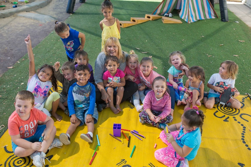 Geraldine Atkinson sits on the floor surrounded by a group of smiling kids.