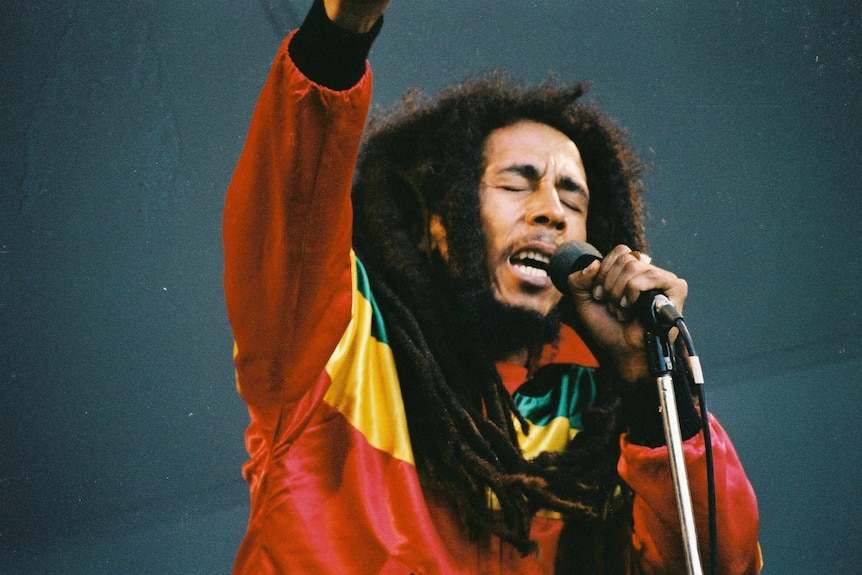 Musician Bob Marley raising a hand in the air while performing on stage in 1980.