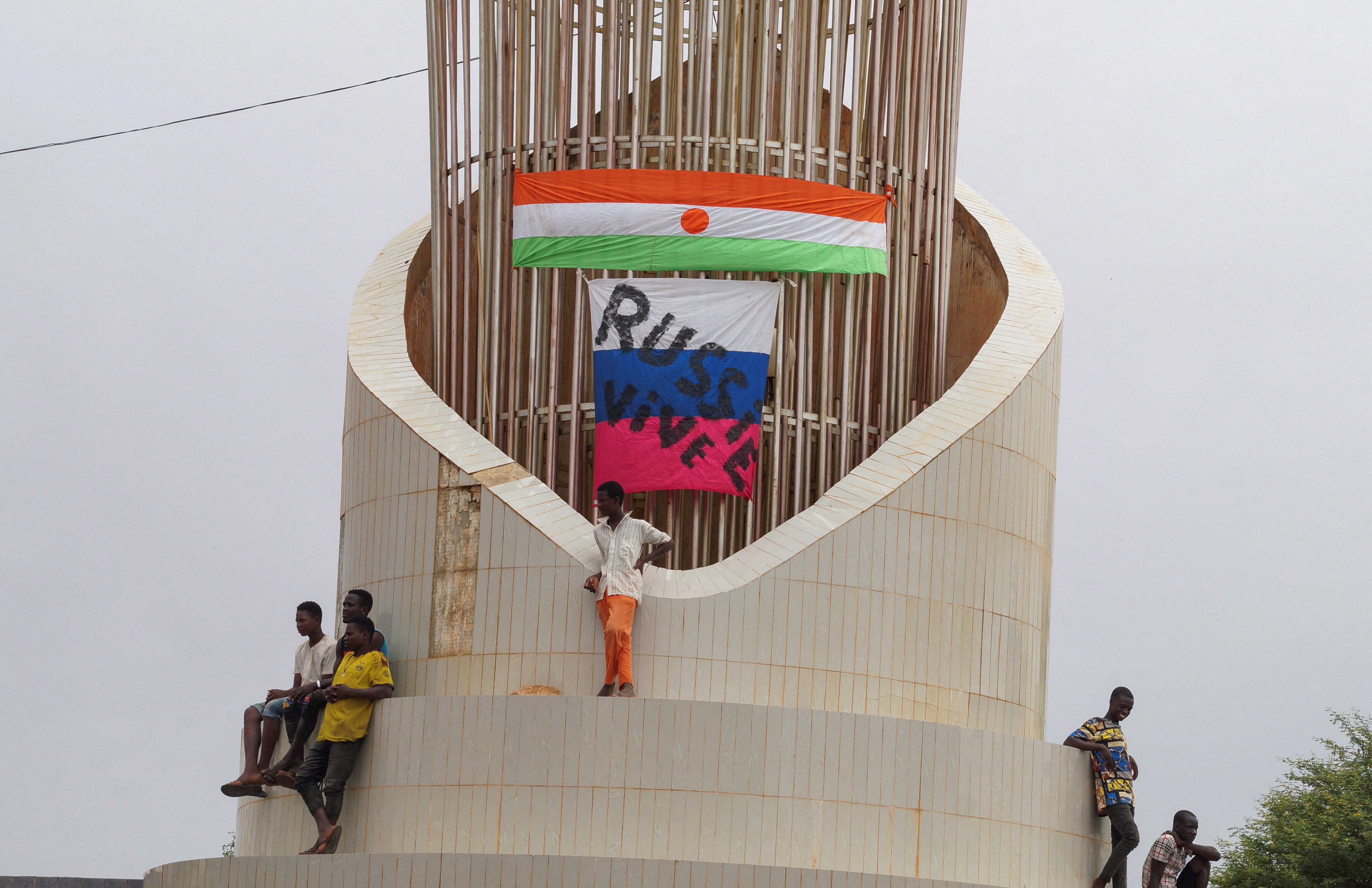 Men stand on top of structure in front of Niger and Russian flags.