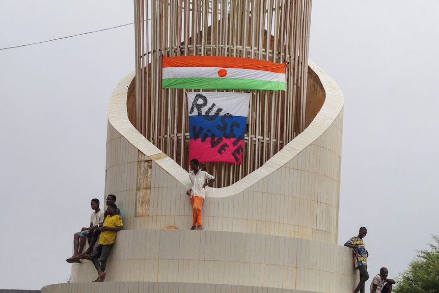 Men stand on top of structure in front of Niger and Russian flags.