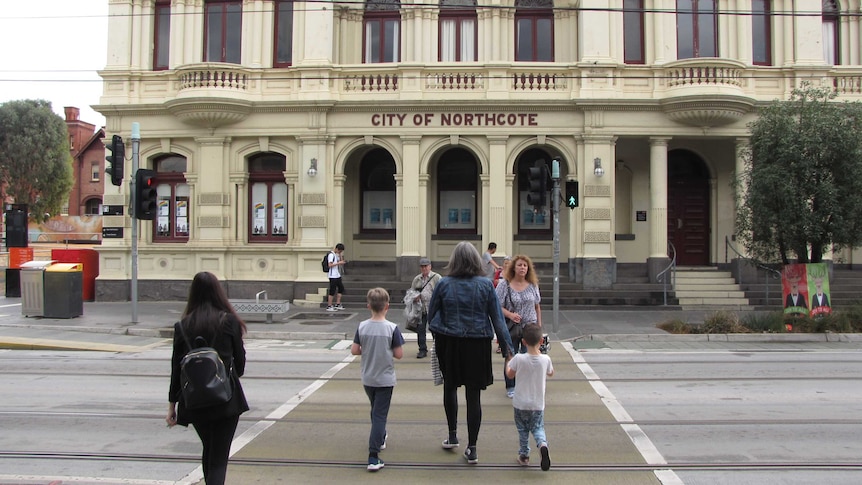 People walking across the street outside the Northcote town hall.