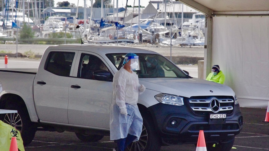 A testing official in protective gear tests a man in a ute.