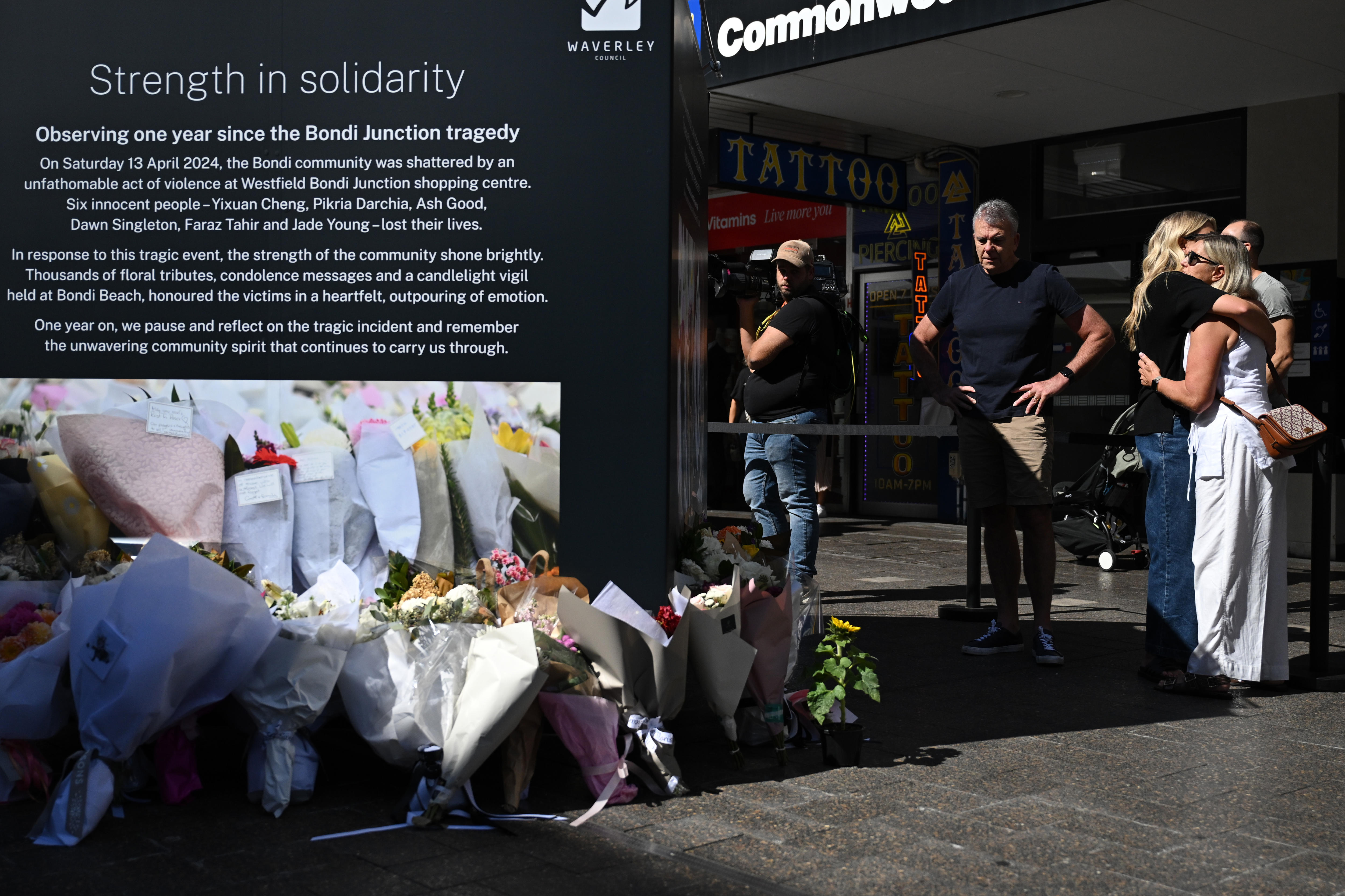 Mourners after embrace after laying flowers at commemorative display boards at bondi junction