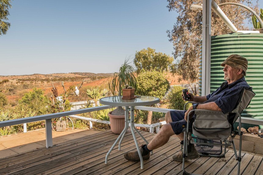 A retiree enjoys a cold drink on his back patio in a rural setting