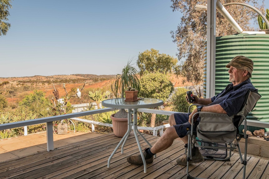 A retiree enjoys a cold drink on his back patio in a rural setting