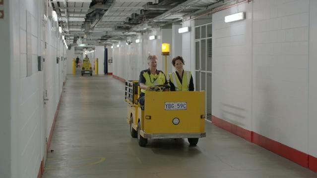 Annabel Crabb and unknown woman ride burden carrier through Parliament House underground corridor
