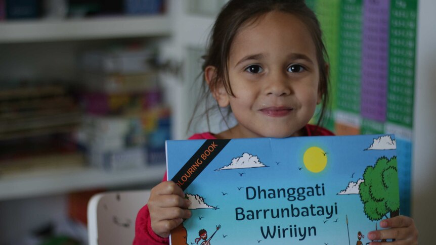 A young girl holds a book and smiles.