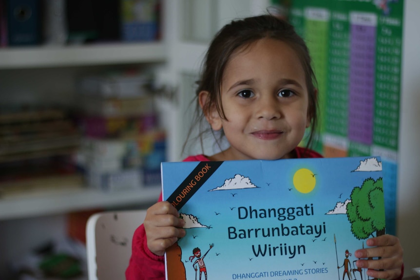 A young girl holds a book and smiles.