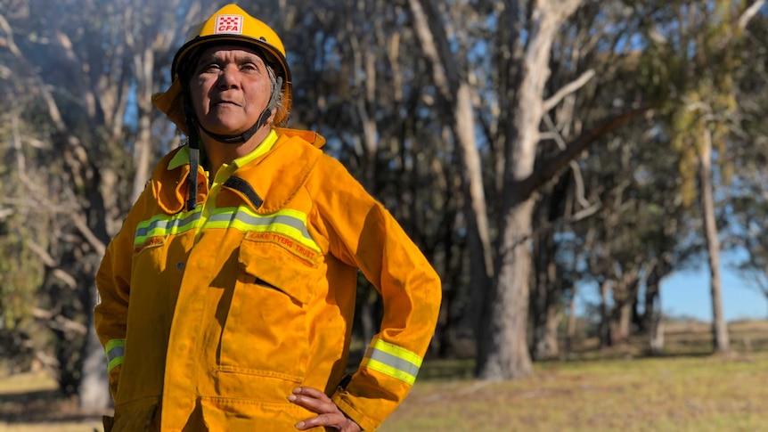 Charmaine Sellings wearing her yellow fire jacket with smoke and bush in the background.