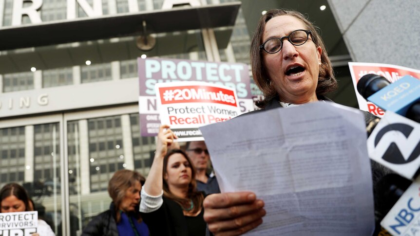 Michele Landis Dauber reads a statement with people petitioning in the background.